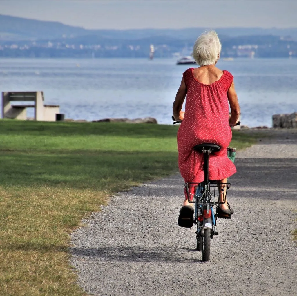 Seniorin auf dem Fahrrad am See – aktives Leben mit dem richtigen Pflegegrad